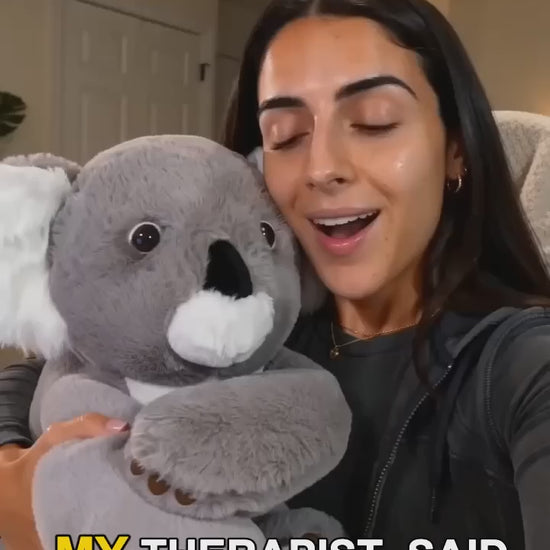 A woman smiling while hugging a large gray weighted koala plush toy 
with white ears and muzzle, sitting in a cozy home setting, with 
on-screen captions about finding comfort.