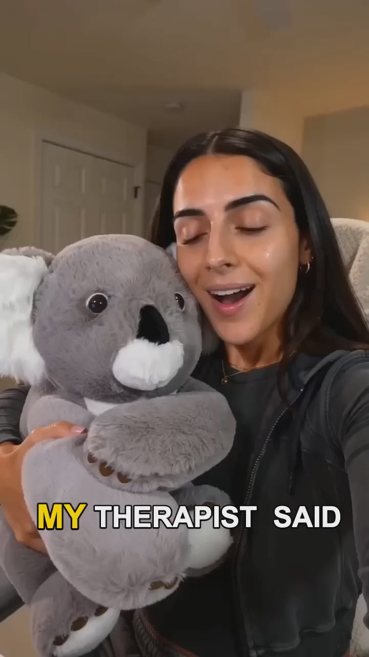 A woman smiling while hugging a large gray weighted koala plush toy 
with white ears and muzzle, sitting in a cozy home setting, with 
on-screen captions about finding comfort.